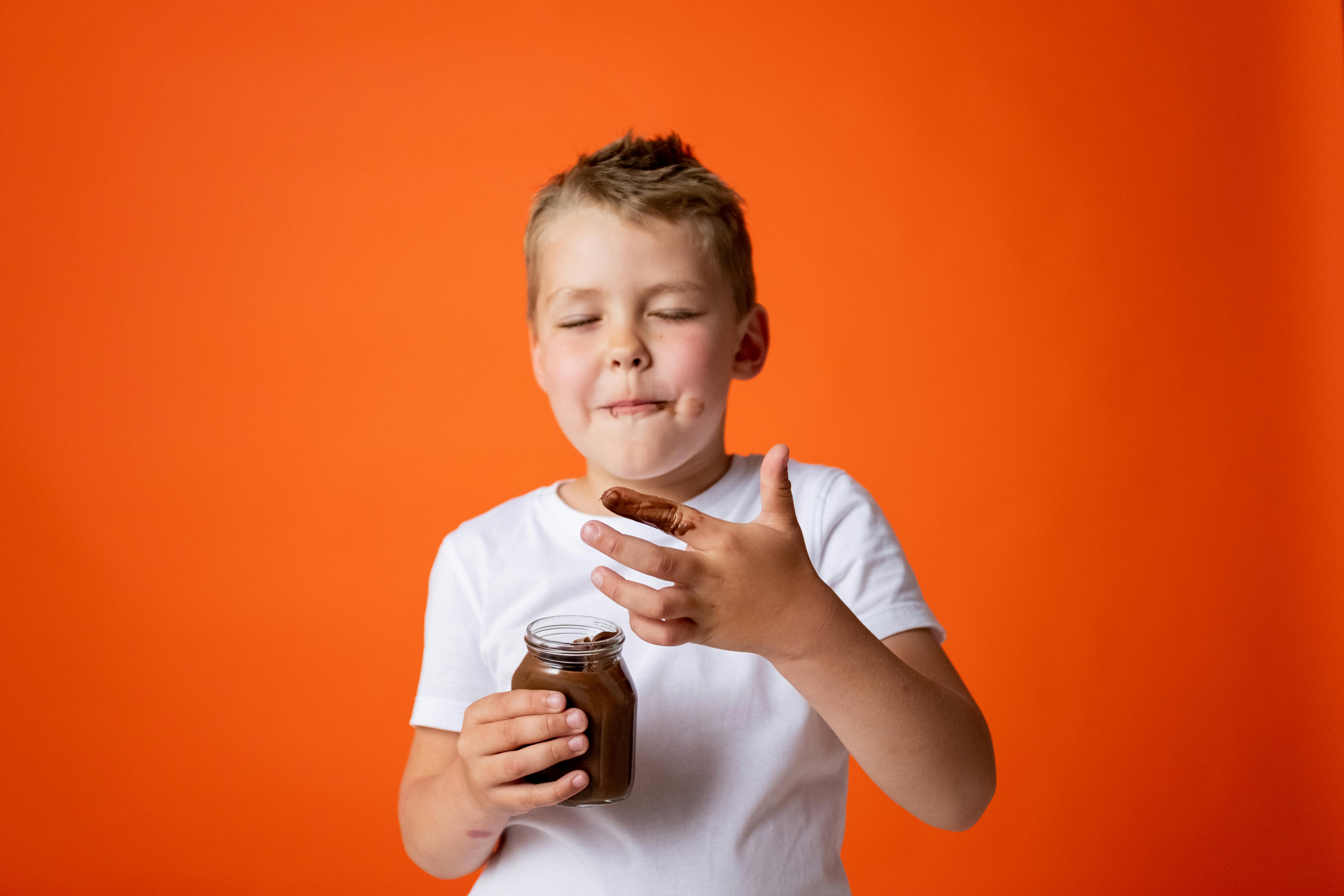 boy in white crew neck t shirt holding chocolate jar