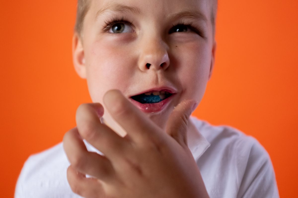 Close-up of a cheerful child with candy against a vibrant orange background, capturing joy and playfulness.