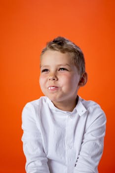 Happy child enjoying candy indoors, wearing a white shirt, with a bright orange background.