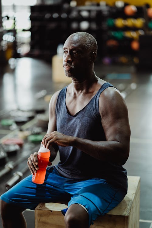 Man in Blue Tank Top Holding Orange Drink in Plastic Bottle