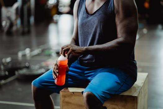 Muscular man taking a break with a sports drink in a gym setting.