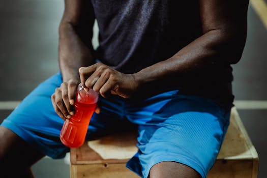 A man resting on a wooden box, enjoying a red sports drink during his workout session.