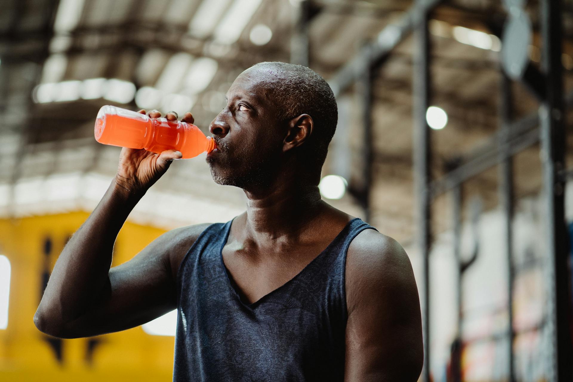 An athletic man enjoys a refreshing energy drink during his workout in a gym setting.