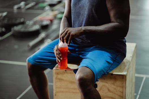 Close-up of a man in a gym holding a sports drink bottle while sitting on a box.