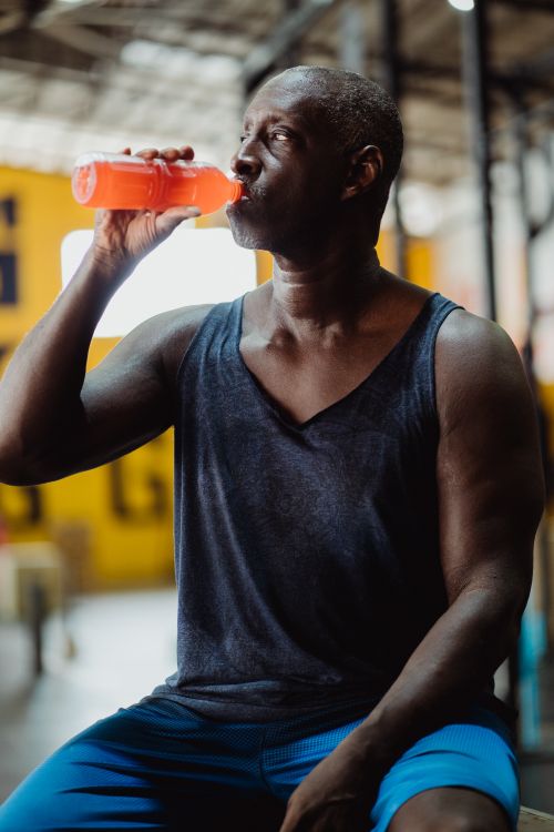 Free Mature African American man drinking a sports drink in a gym, showcasing fitness and hydration. Stock Photo