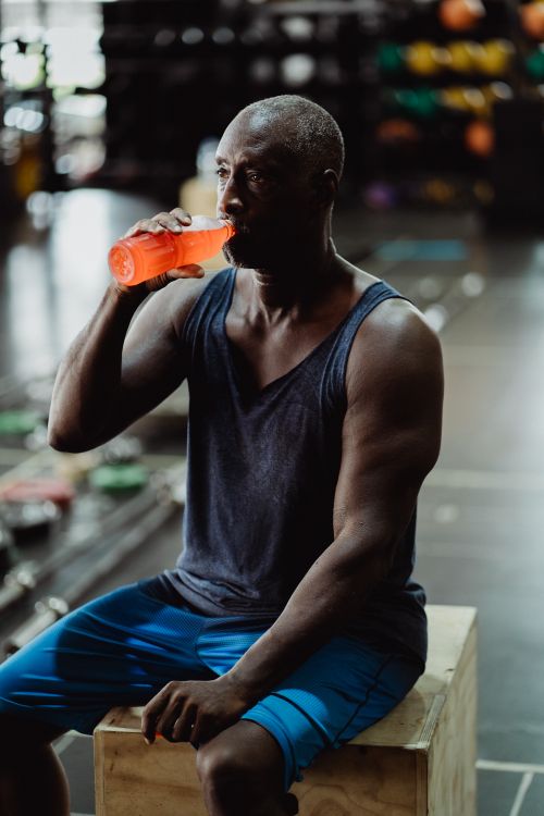 Free Mature African American man drinking juice during a gym workout session sitting on a wooden box. Stock Photo