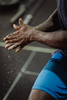 Close-up of an athlete clapping chalked hands before exercise in the gym.