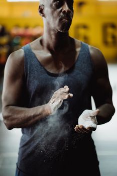 Muscular man preparing for workout by clapping chalk on hands in an indoor gym setting.