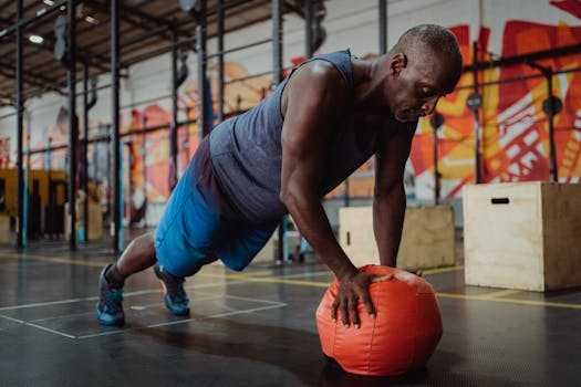 An athletic man doing push-ups on a medicine ball in a colorful gym setting.