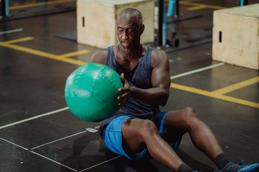 A mature man in a gym performs a workout with a green medicine ball, focused on exercise.