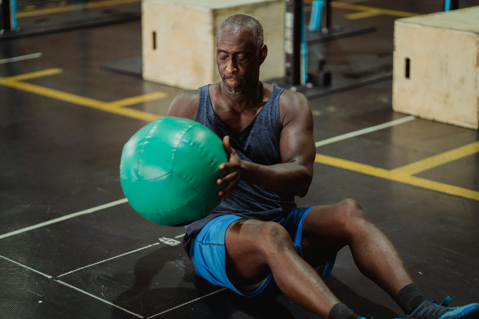 A mature man in a gym performs a workout with a green medicine ball, focused on exercise.