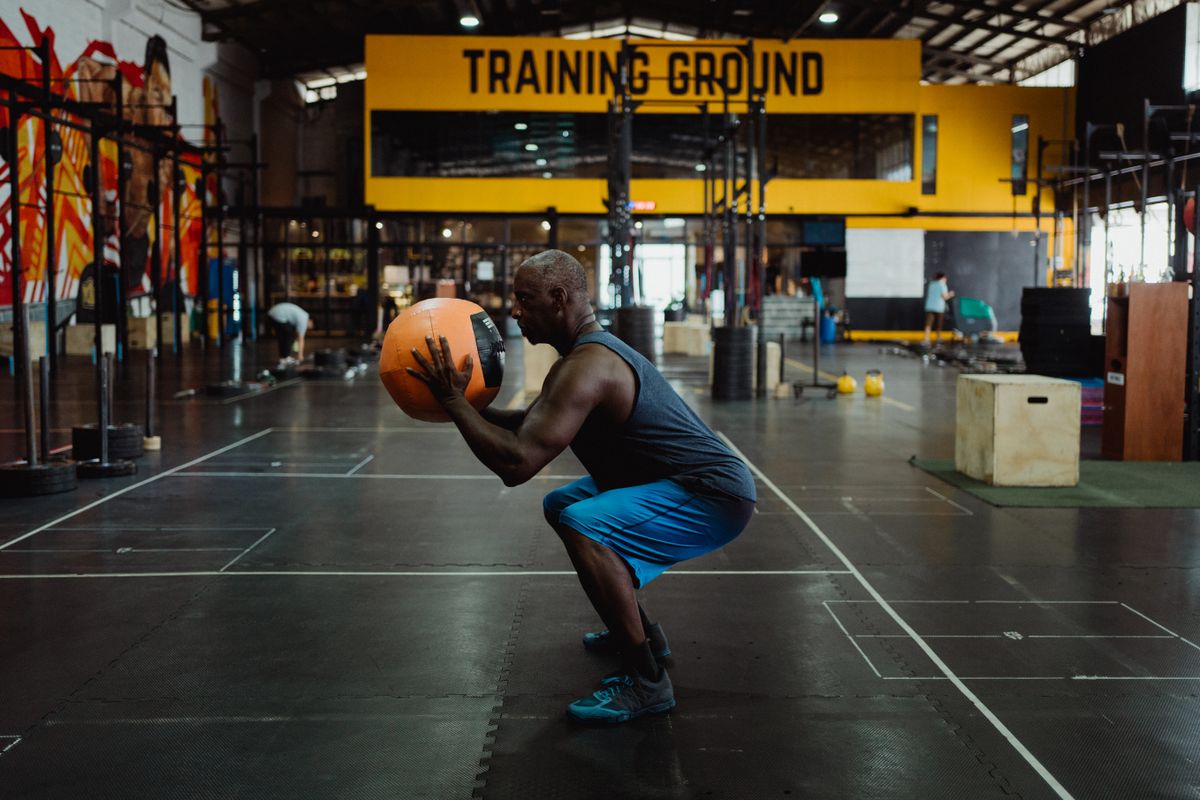 Man performing a squat exercise with a medicine ball in a gym