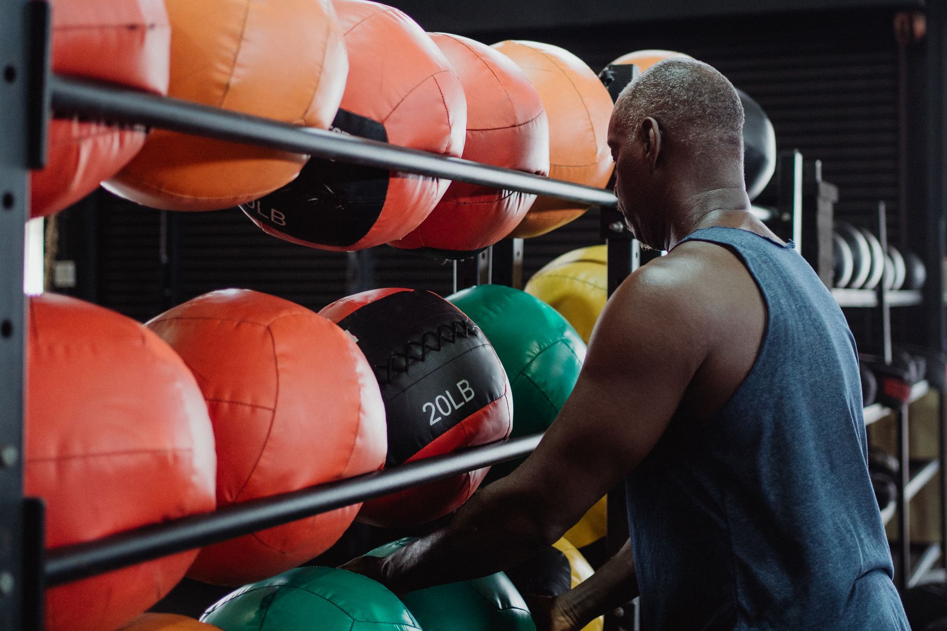 Athletic man selecting a 20-pound medicine ball for his fitness routine in a modern gym setting.