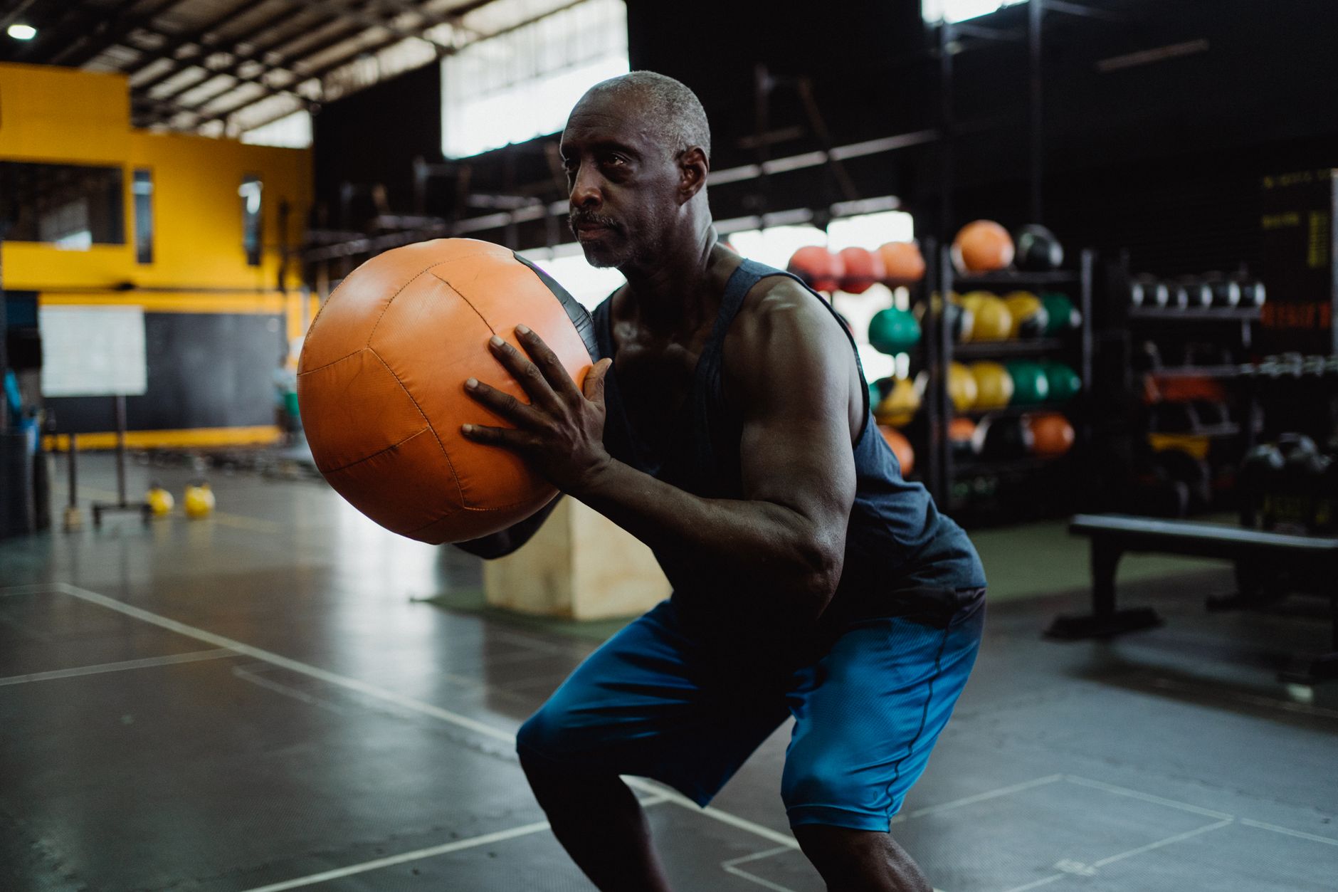 Focused mature man in gym squatting with a medicine ball during a workout.