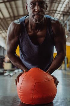 An athletic senior adult man performs an intense workout using a medicine ball in a gym setting.
