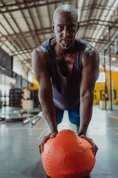 Senior adult performing push up exercise with medicine ball in gym setting.