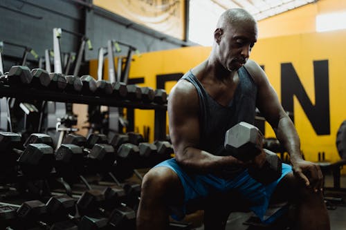 Man in Blue Tank Top and Shorts Exercising With a Dumbbell on Bench