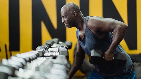 Strong senior man focusing on strength training with dumbbells in a vibrant gym.