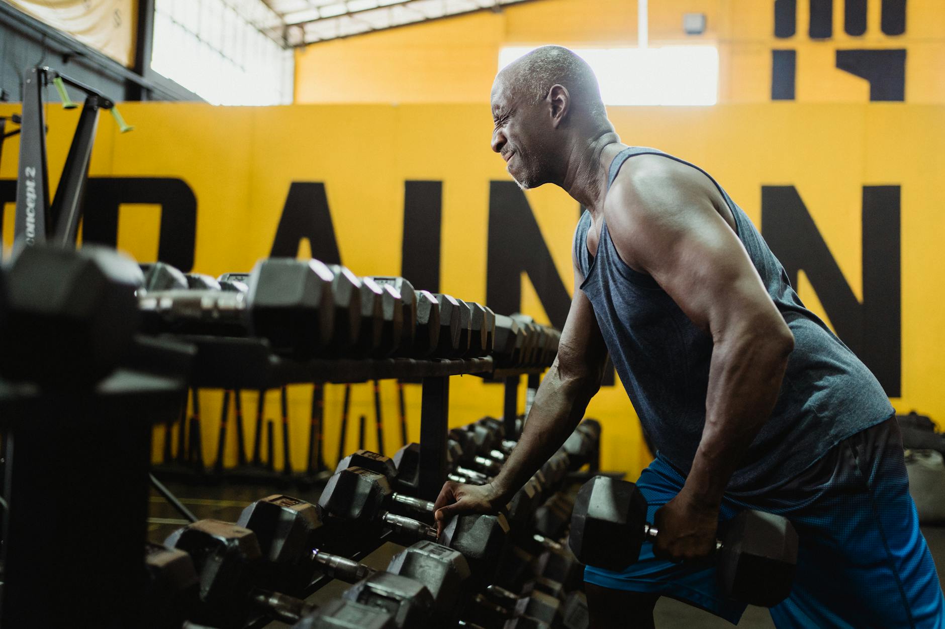 Man in Blue Tank Top Lifting a Heavy Dumbbell