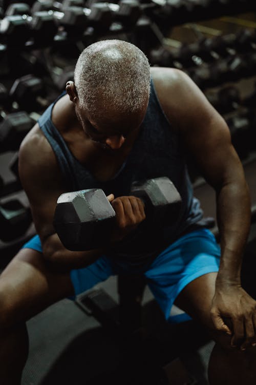 Man in Blue Tank Top Lifting a Black Dumbbell on Bench