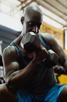 Muscular man lifting dumbbells during an intense workout session in a gym environment.