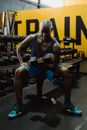 Man in Blue Tank Top and Shorts Sitting on Bench Lifting a Dumbbell
