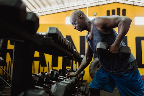 Man in Blue Tank Top Exercising by Lifting a Dumbbell