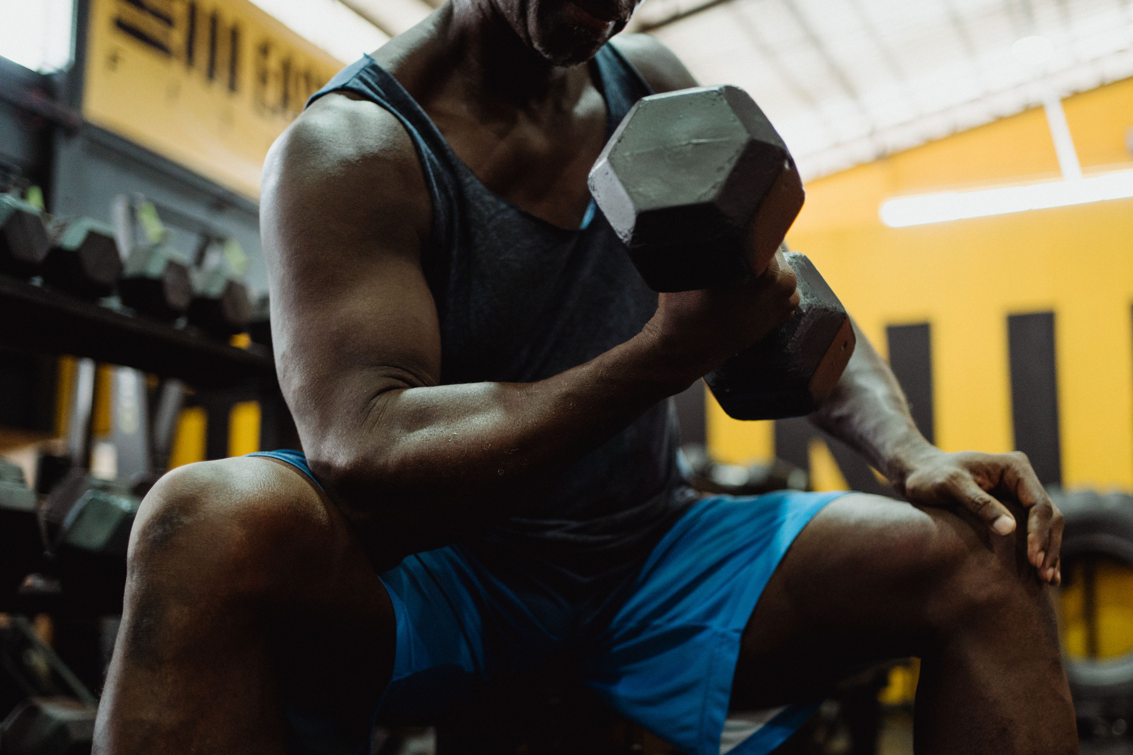 Close-up of a muscular man lifting dumbbells in a gym for strength training.