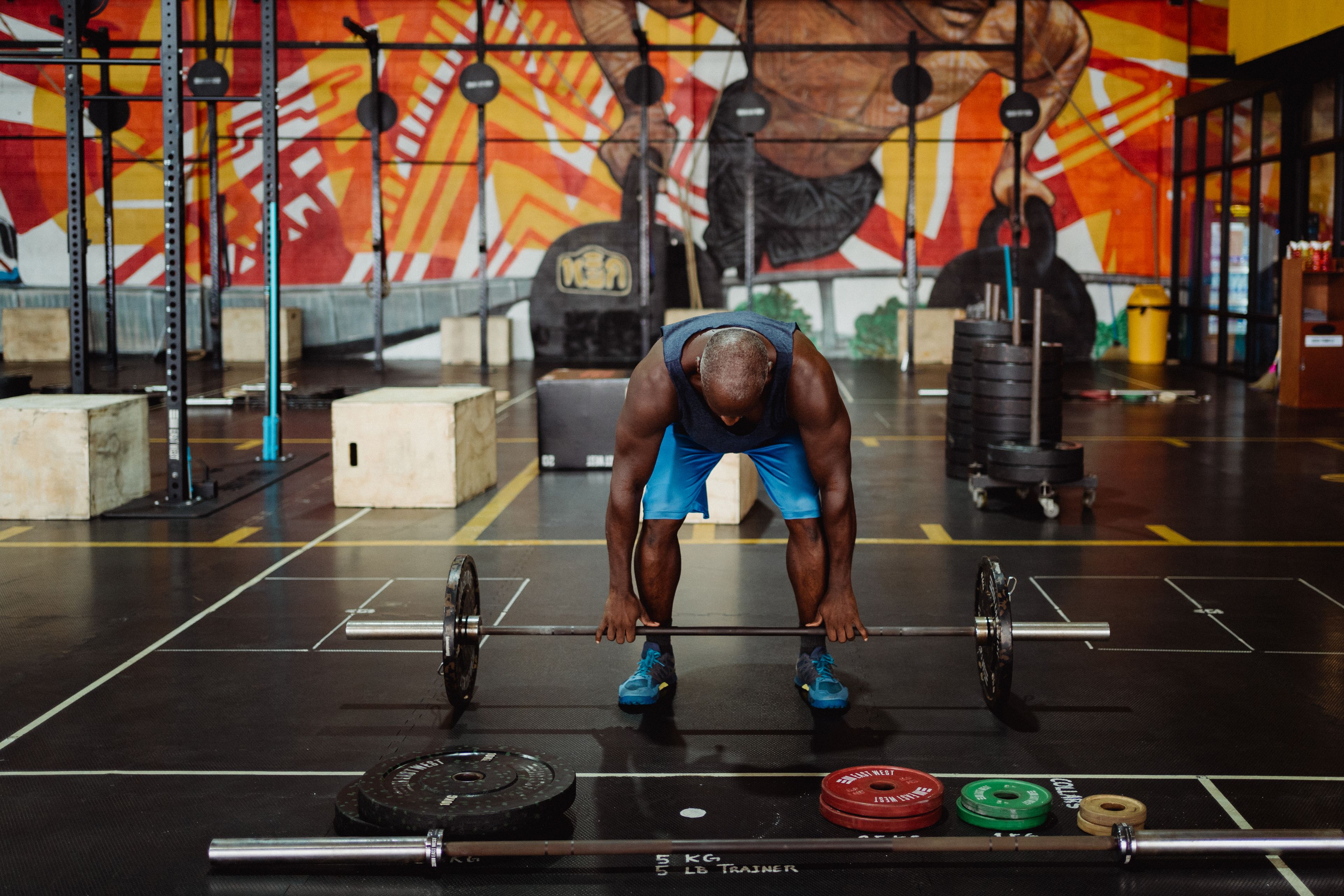 A muscular man lifting a barbell in a colorful gym setting, emphasizing strength and fitness.