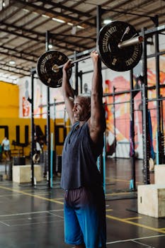 Adult male engaged in strength training with barbell in contemporary gym setting.