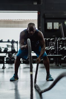 Athlete performing a strength workout with battle ropes in a dimly lit gym.