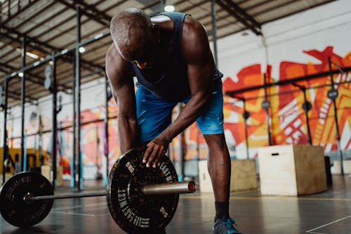 Man in Blue Shorts Holding Black Barbell