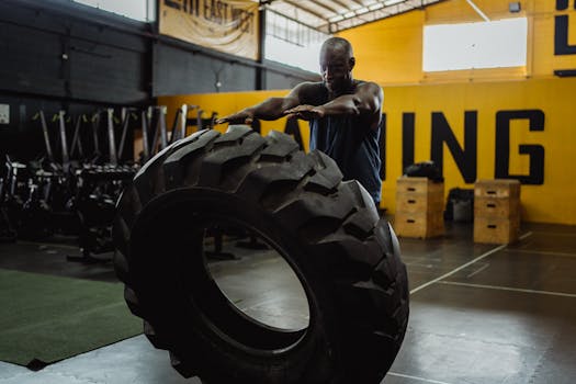 Man engaged in flipping tire exercise at gym, showcasing strength and fitness.