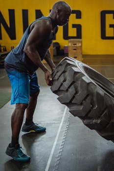 An athletic man flips a large tire during an intense gym workout session.