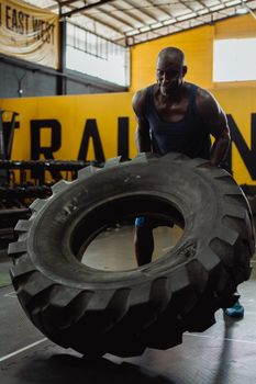 Strong man flipping heavy tire in an industrial gym environment, showcasing strength and fitness.