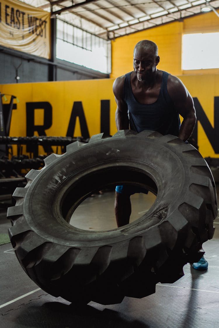 Man In Blue Tank Top And Shorts Flipping A Tire