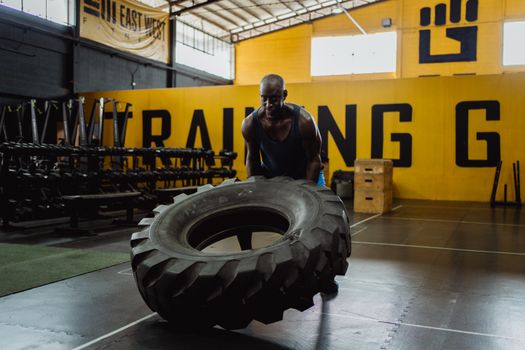 A fit man flipping a large tire inside a gym, showcasing strength and endurance.