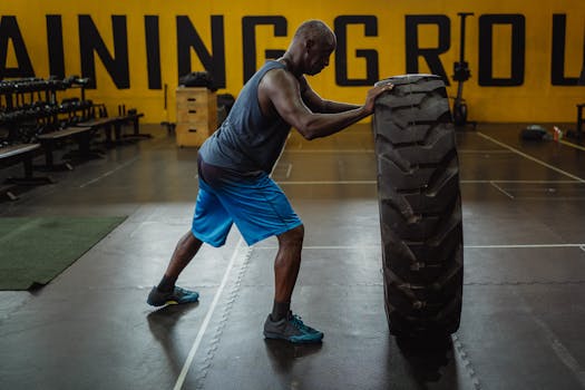 A man pushing a large tire in a gym, showcasing strength and endurance in an indoor workout setting.