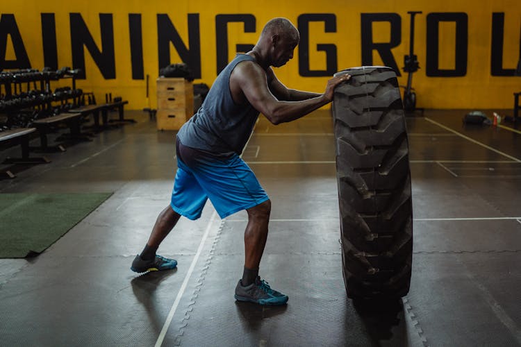 Man In Blue Tank Top And Blue Shorts Doing Tire Training Exercise