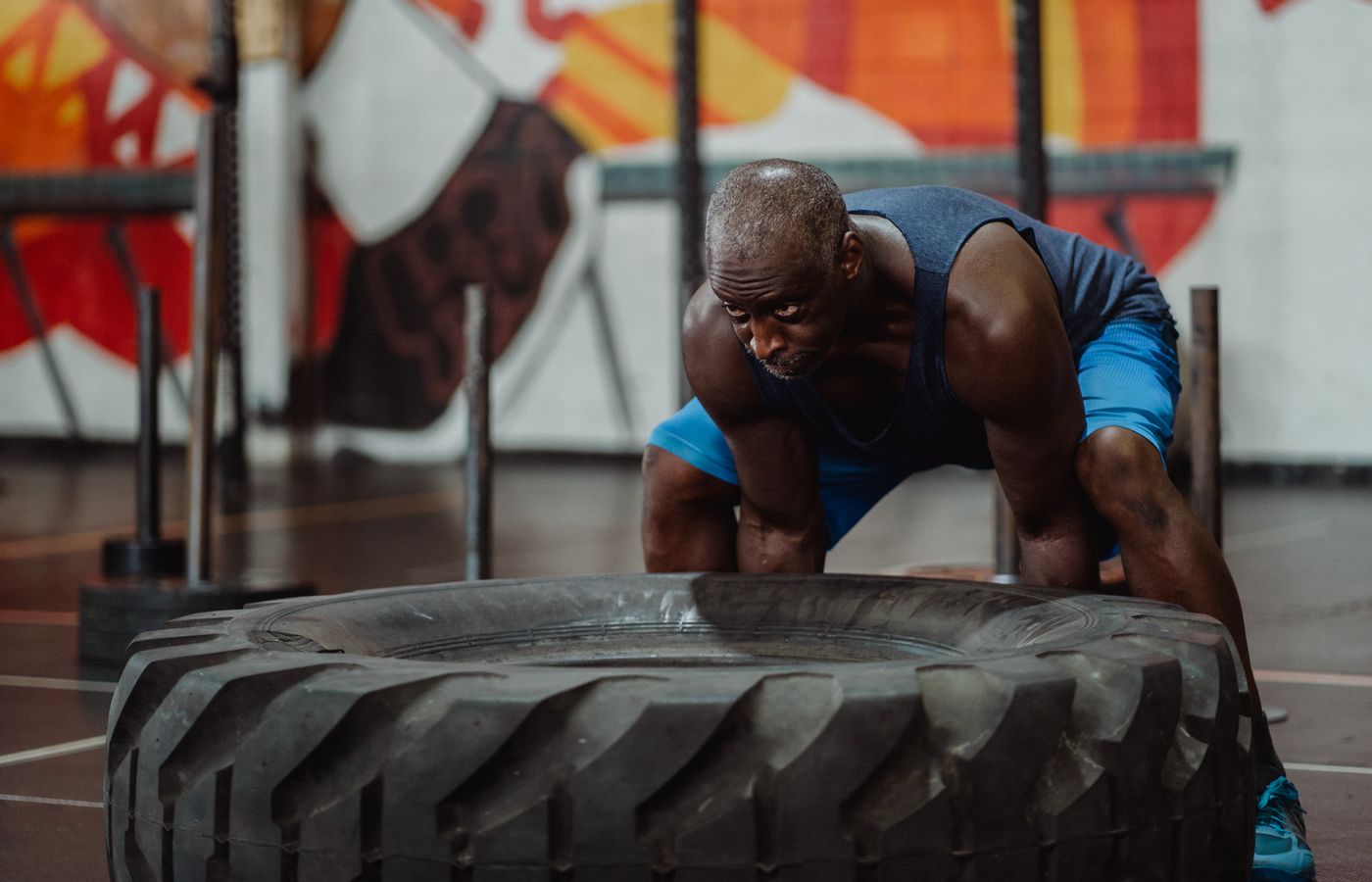 An athletic man engaged in a strength workout, flipping a large tire in a gym.