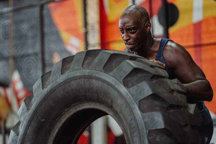 Man In Blue Tank Top Pushing A Tire