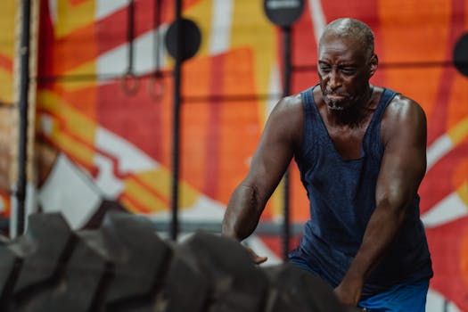 Muscular black man in tank top flipping a tire in an urban gym setting.