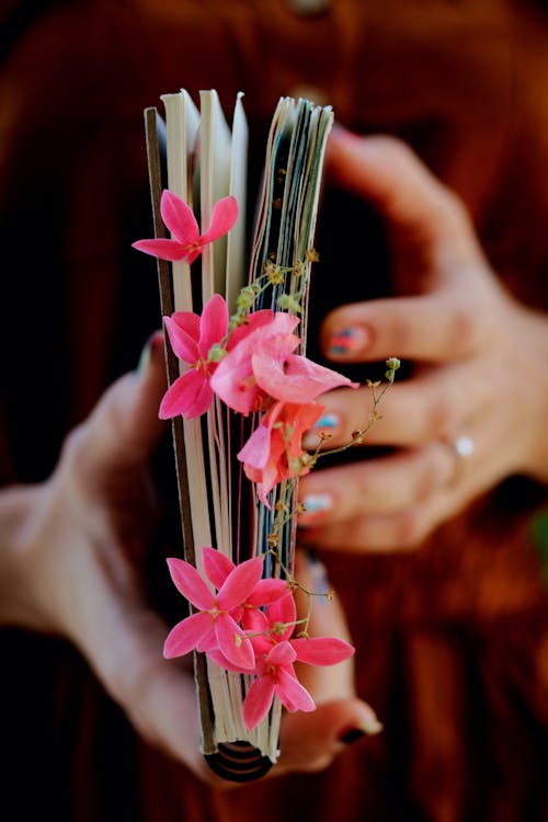 Crop anonymous female holding book decorated with blooming bright flowers placed between pages