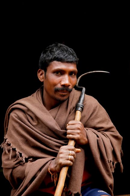 A tribal man in traditional attire holding a sickle in Araku Valley, India.