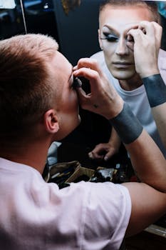 A drag performer meticulously applies eye makeup while looking in a mirror, capturing the art of transformation.