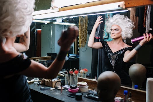 A drag performer in a glamorous black dress preparing in front of a mirror.