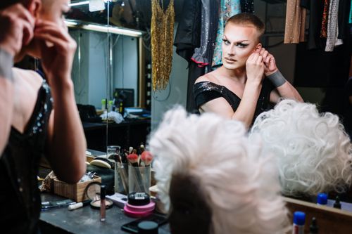 Free A drag performer gets ready in a dressing room, applying makeup and adjusting earrings. Stock Photo