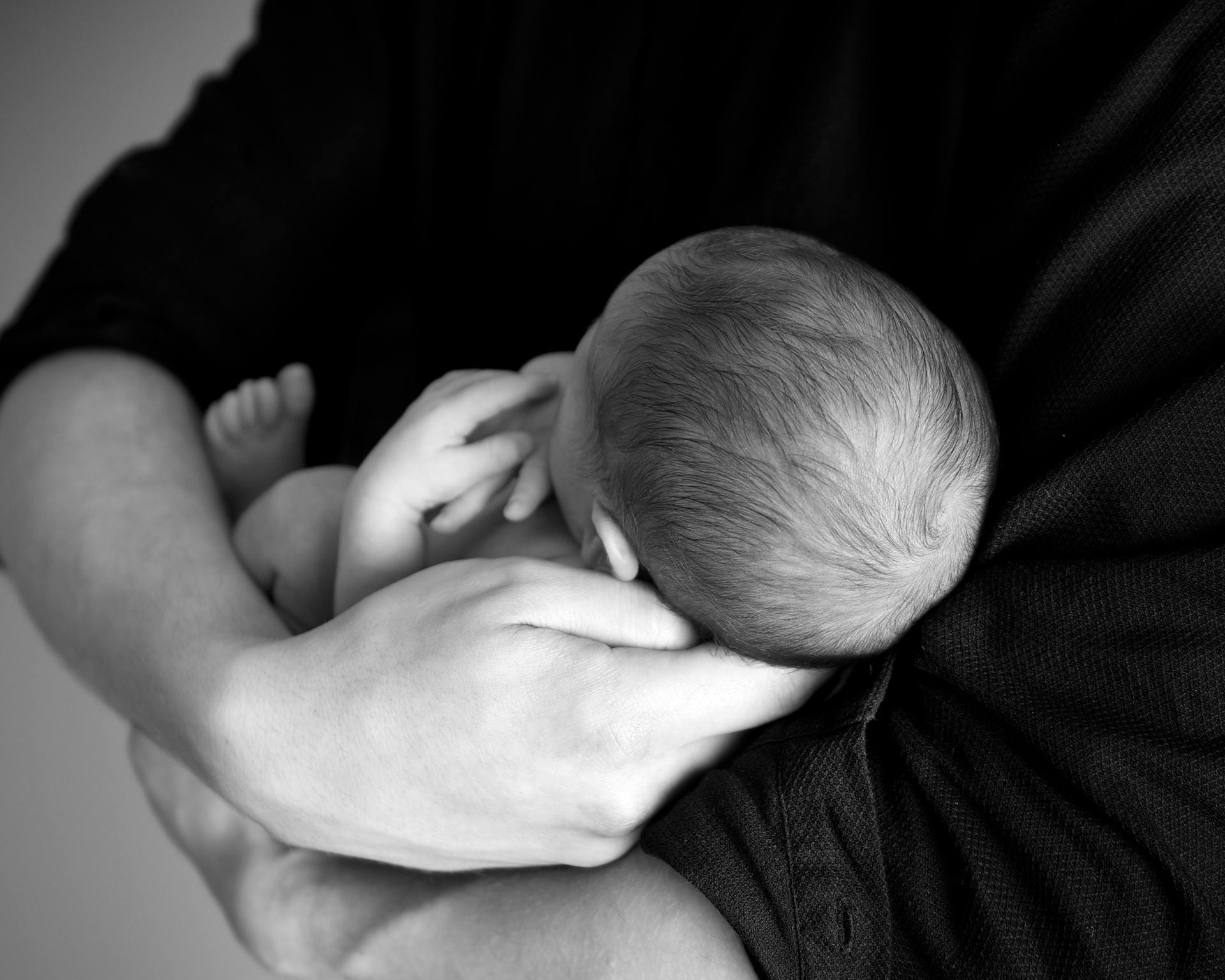 A black and white close-up of a parent holding a newborn baby in arms, conveying love and care.