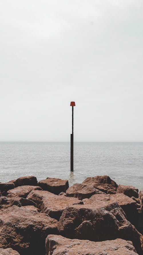 Black and Red Lamp Post on Body of Water Near Brown Rocks