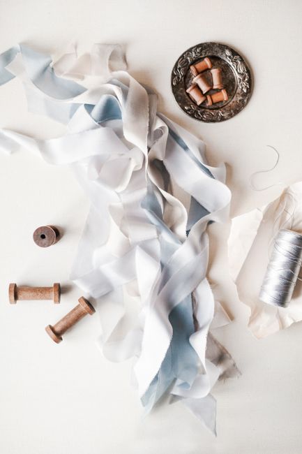 Top view of white and light blue ribbons between simple empty spools on plate and spool of white threads in daylight on white background